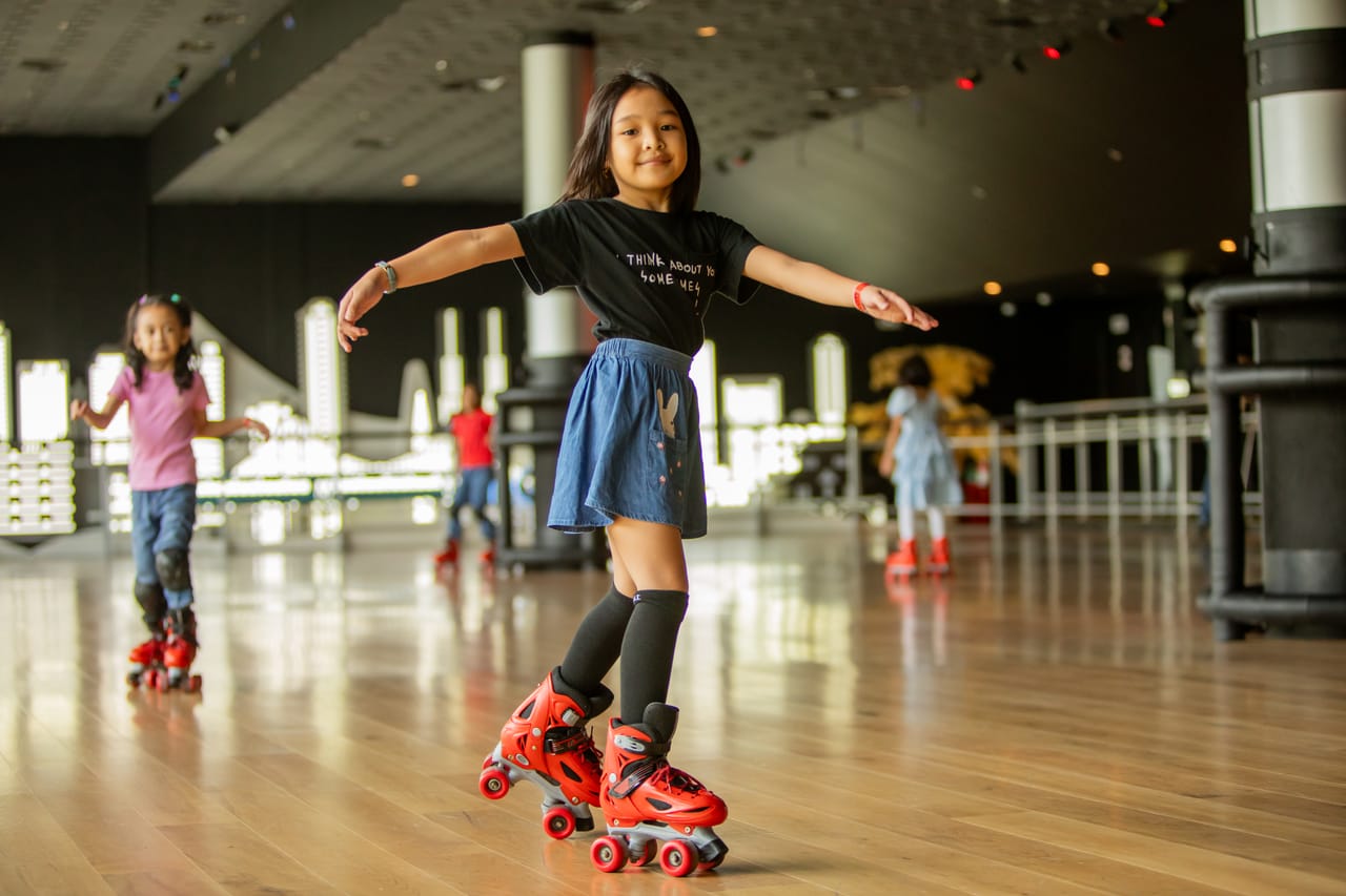 A girl glides with her arms out on red roller skates while other kids skate around the Spin City rink